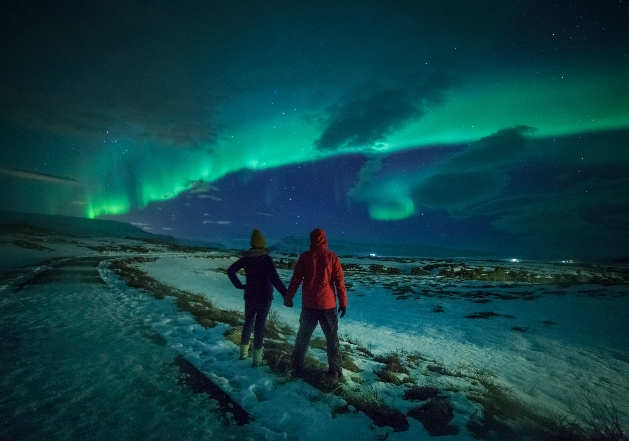 A couple holding hands in front of the Northern Lights