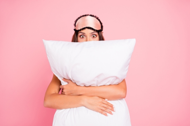 Lady in pink eyemask hugs a white pillow