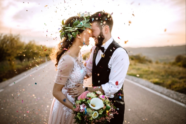 Couple stood in the road laugh whilst being showered in confetti