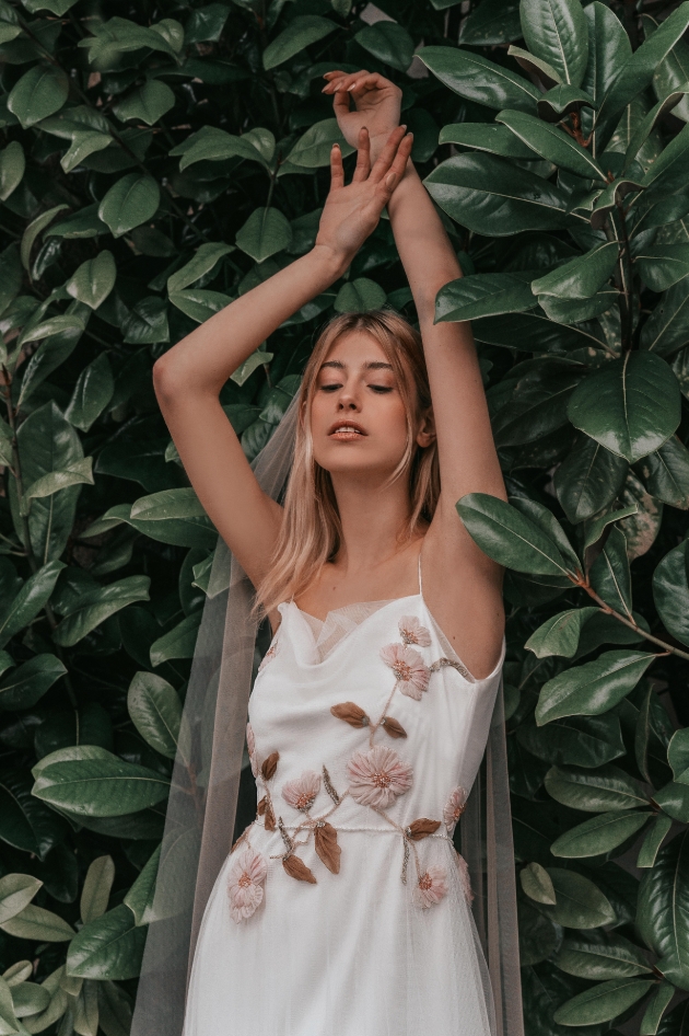 Model standing in the garden with her hands in the air wearing a wedding dress with flower detail