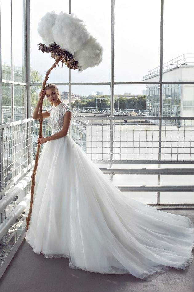 Bride standing inside a glass building holding huge flower as a prop while wearing a wedding dress