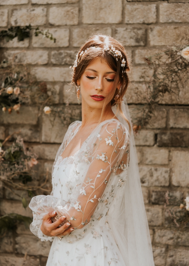 Model wears dress with see-through sleeves with flower detail 