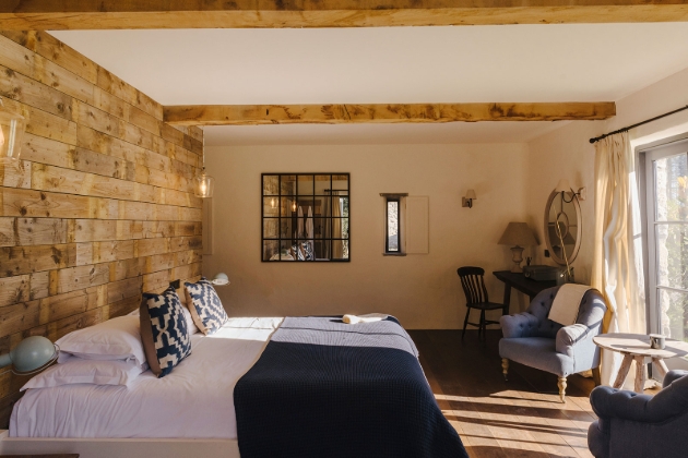 Bed in a room with arm chair and dressing table with a wood-panelled wall and french doors