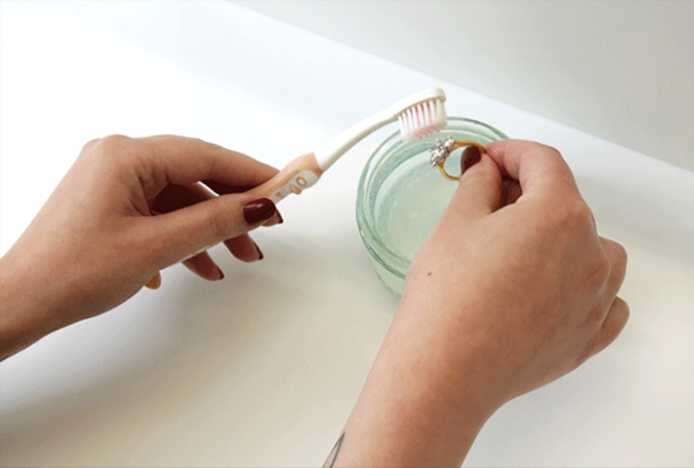 Hands holding toothbrush cleaning a diamond ring