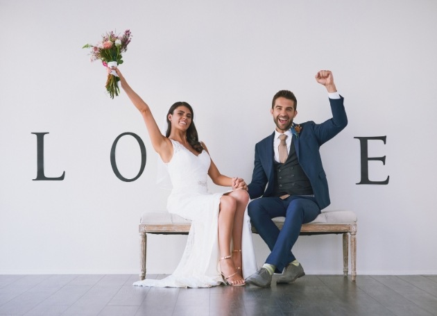 couple on bench cheering in wedding outfits