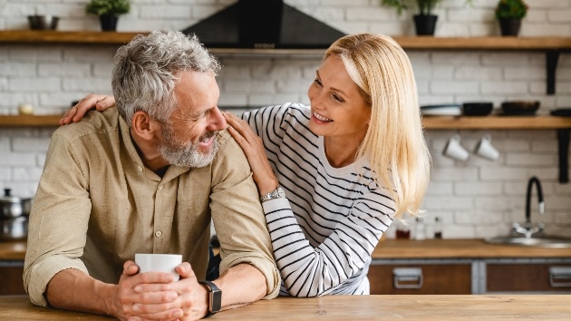 older couple leaning on kitchen table embracing 