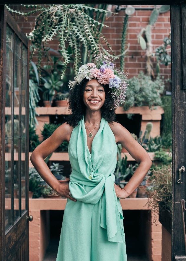 Hazel Gardiner in green dress and wearing flower crown in front of garden shed