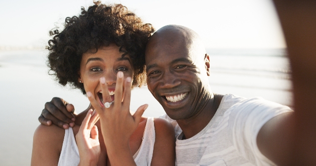 couple on beach posing to camera with ring on hand