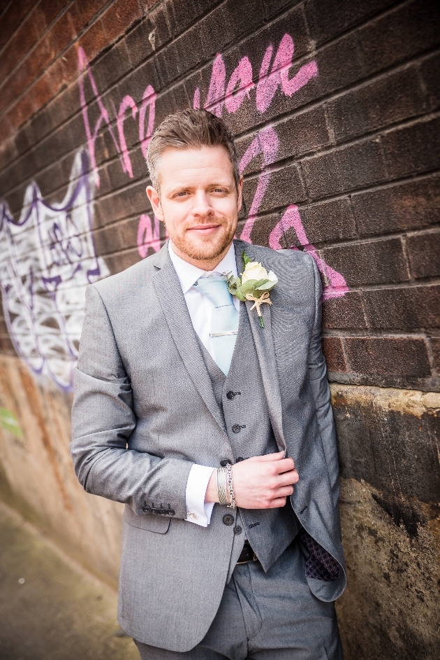 Groom leans up against a brick wall