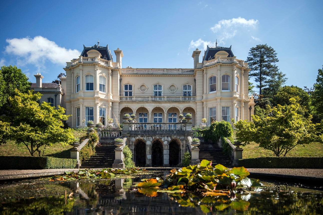 historic white building of hotel stands above a pond and formal gardens