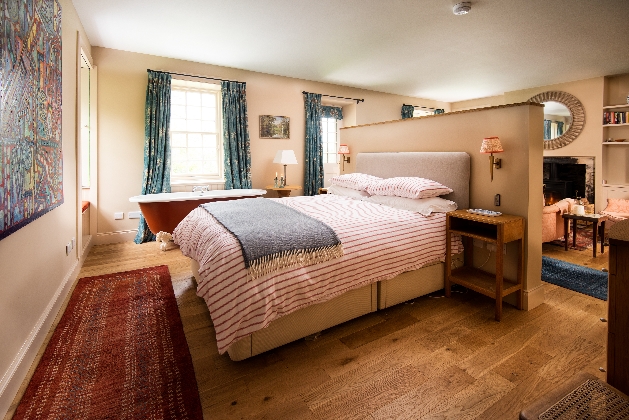 red roll top freestanding bath, next to large comfy bed on the back of a room divider 