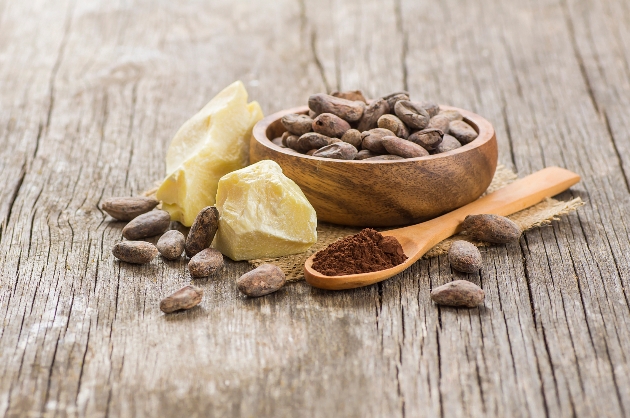 Cocoa butter or Cocoa bean solid oil with cacao powder in spoon and raw cocoa beans in wooden bowl on rustic backdrop, healthy natural oil