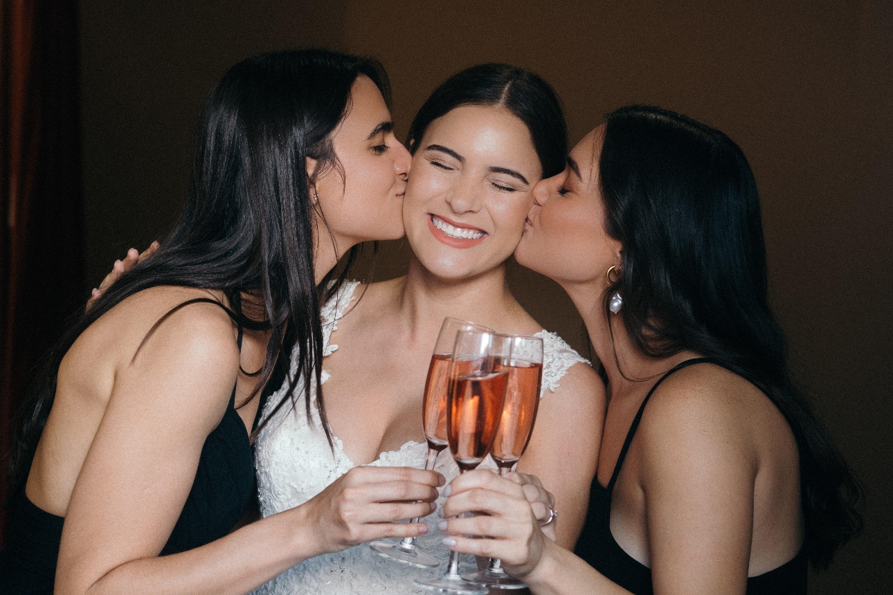 bride and bridesmaids kissing her on cheek all holding wine glasses