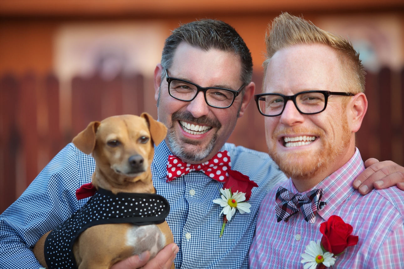 two men in bow ties and shirts holding a dachshund in a bow tie