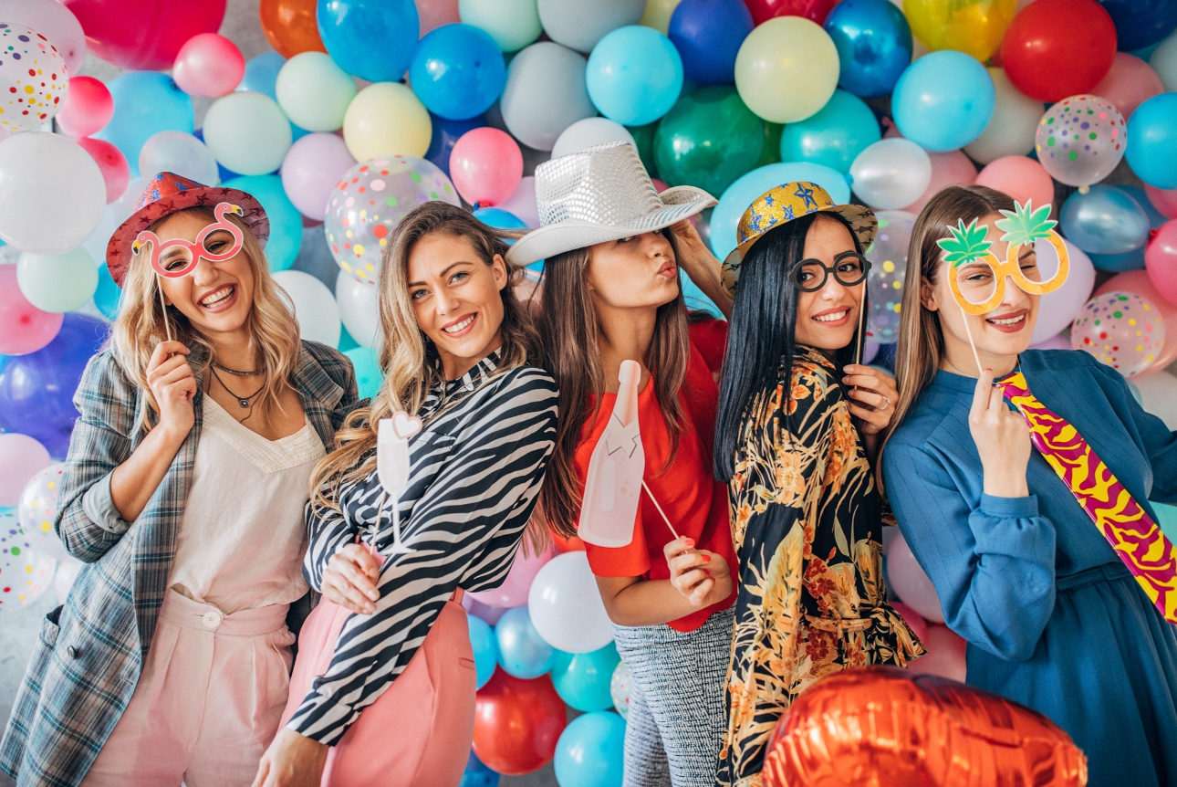 five woman dressed up for a party holding photo booth props