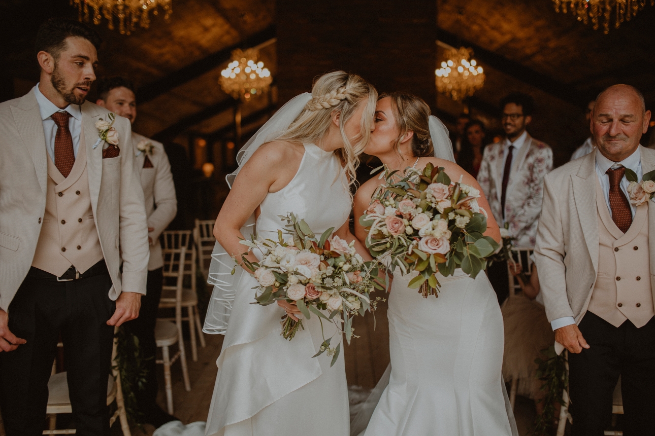 bride and bride kissing at the end of the aisle in front of their guests