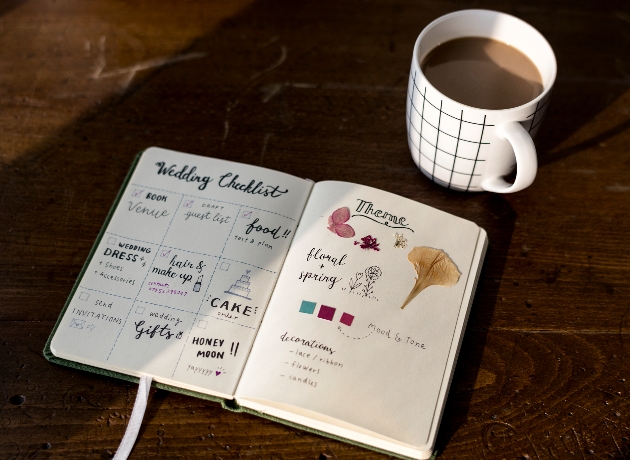 wedding planning diary with lots of notes on it on a table with a mug of coffee