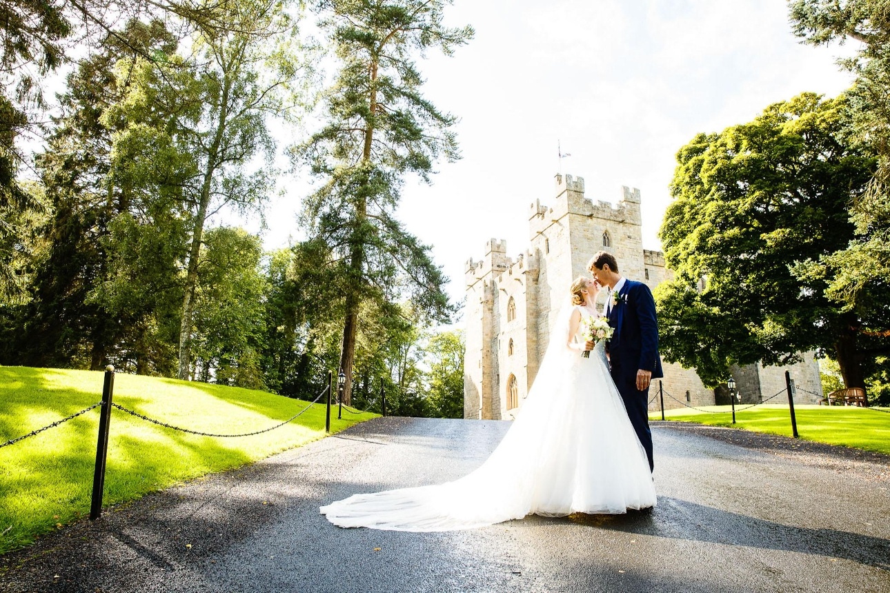 bride and groom standing on a drive in front of a castle