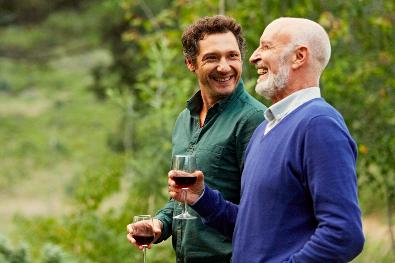 two men in a vineyard drinking wine and laughing