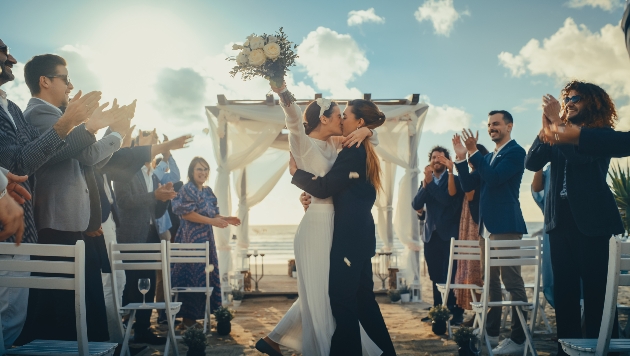 bride and bride just wed on a beach surrounded by guests