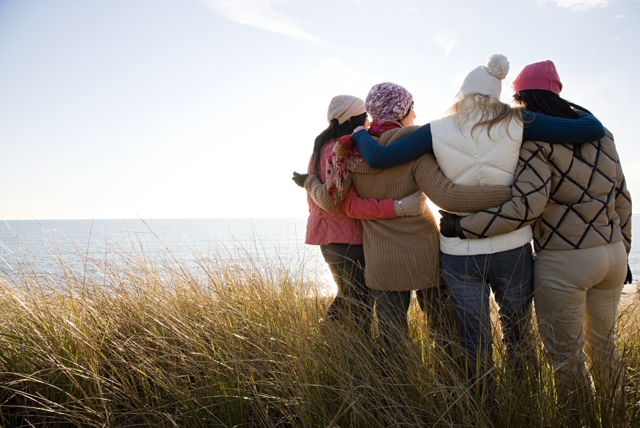 group of friends in winter coats taking a walk on a beach