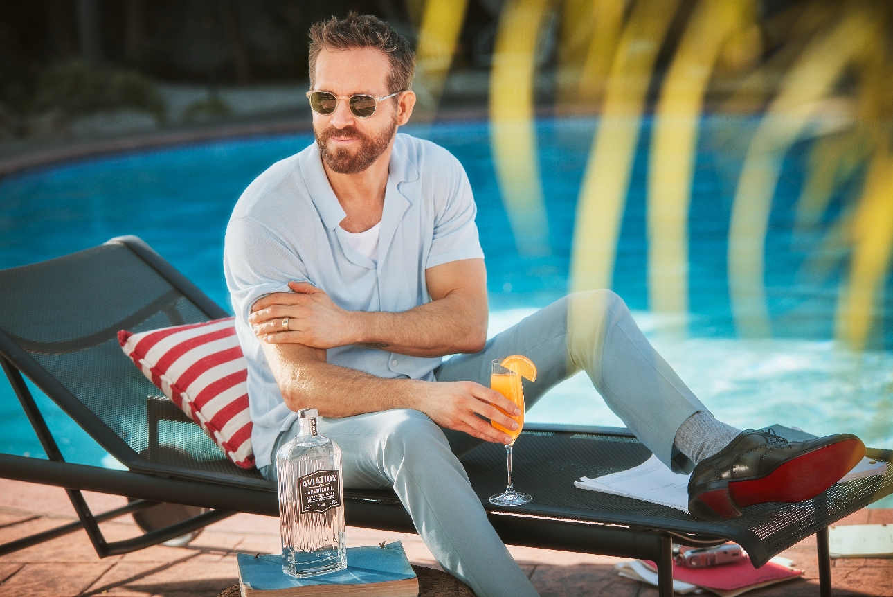Ryan Reynolds on a pool lounger with sunglasses on a holding a cocktail