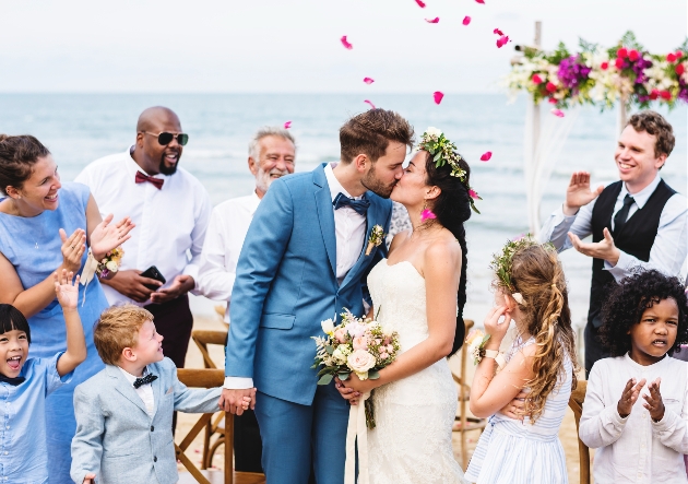 two people tying the knot on a beach with guests