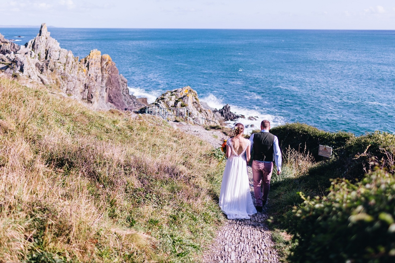 Bride and groom walk down cliff path