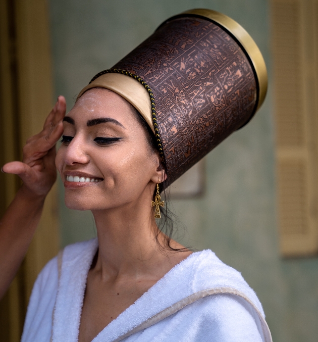 Women dressed in ancient Egyptian attire smiling as she has a facial