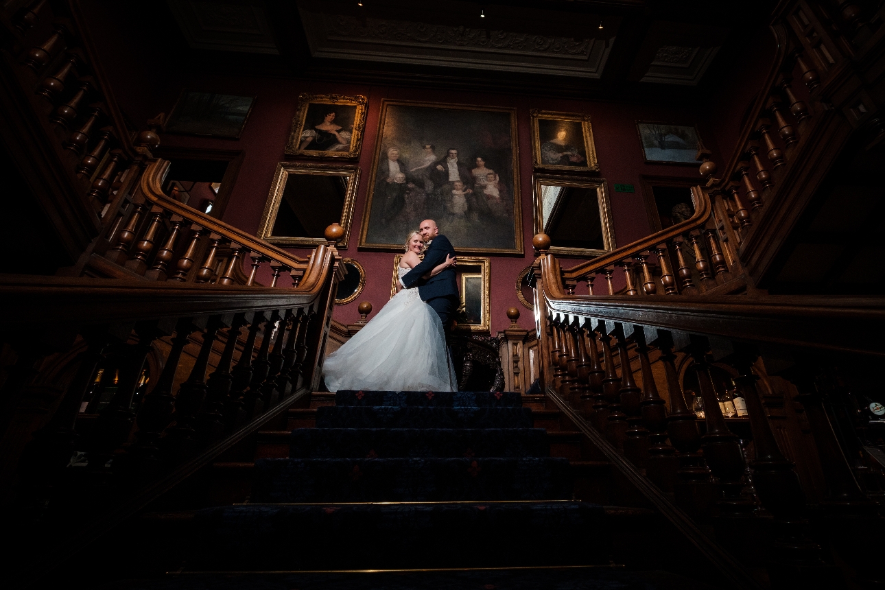 bride and groom stood at top of stairs in stately home with ornate artwork on the walls