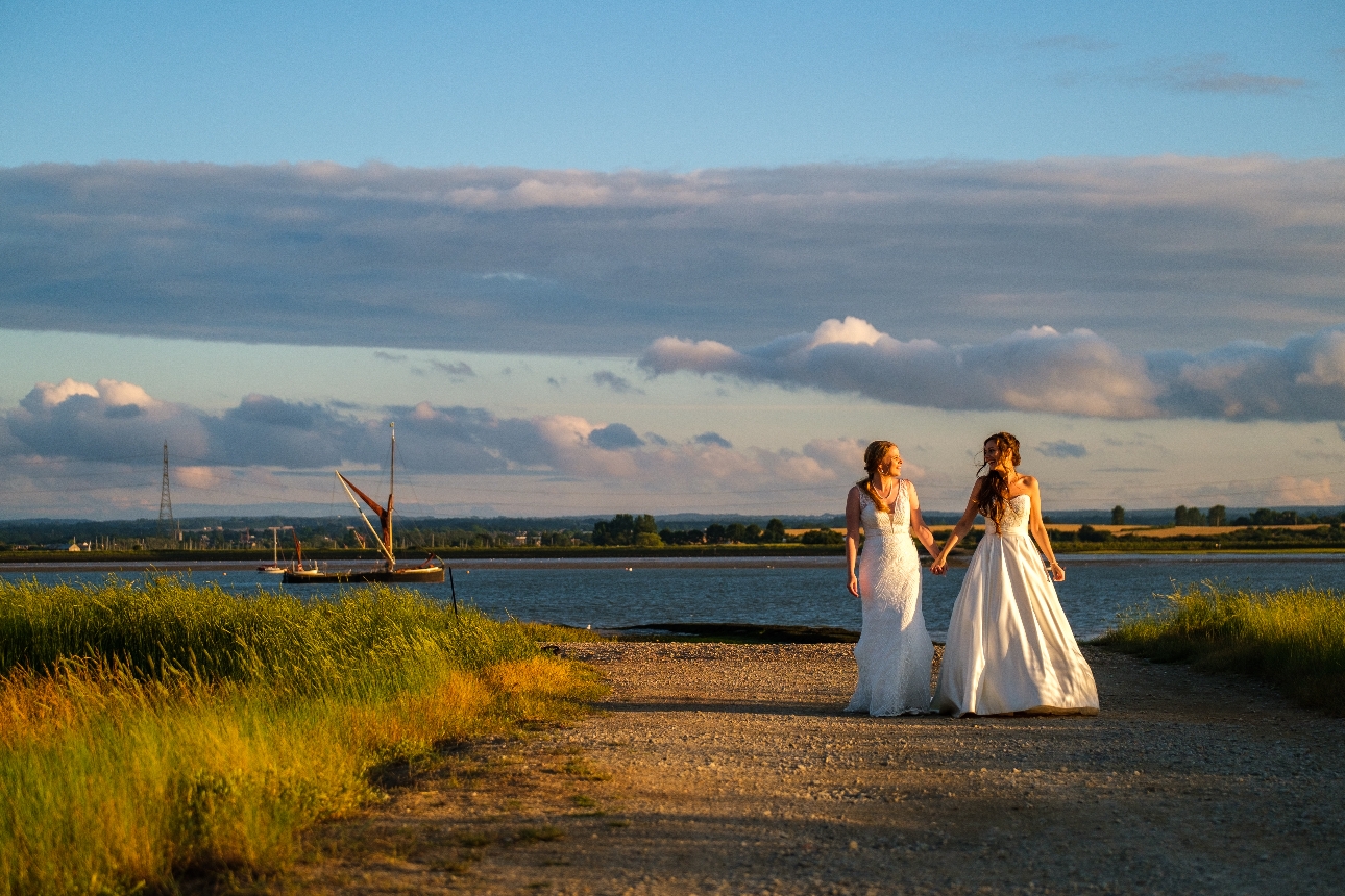two brides walking down a sand beach path at sunset