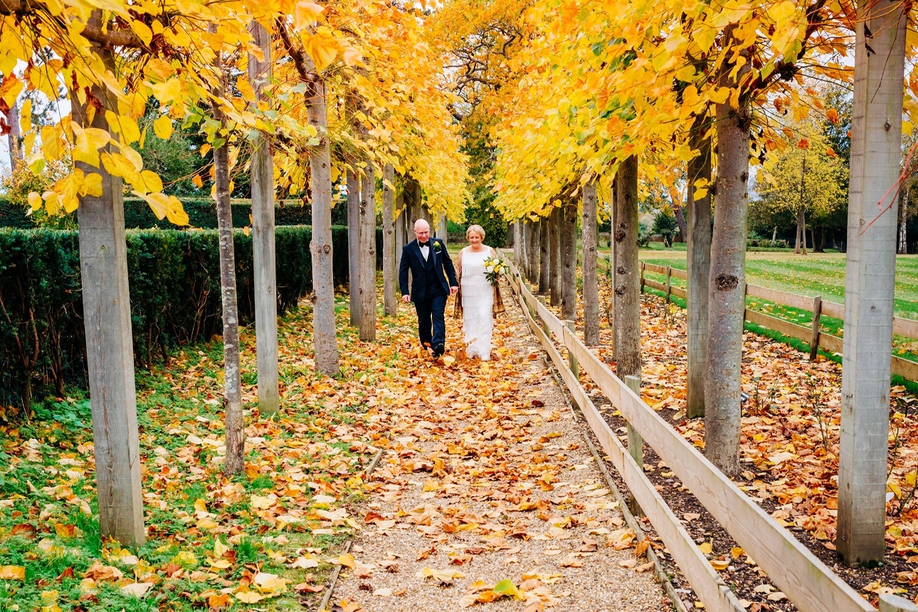 Bride and groom walk under autumn leaves