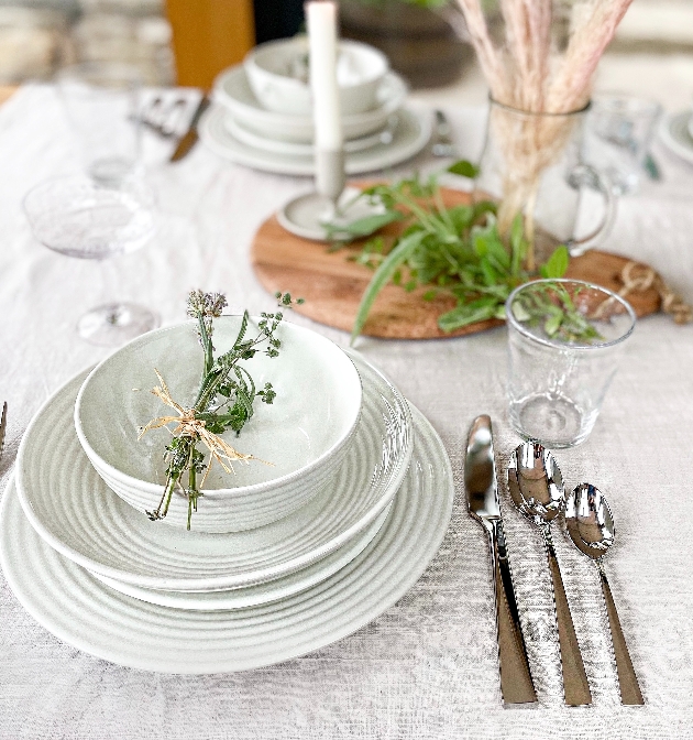pale green plates and bowls set at a table with rustic wood platters and silver cutlery 
