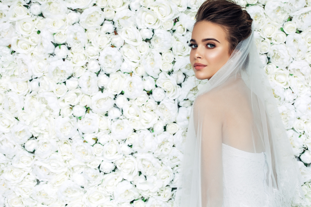 model bride in veil posing in front of flower wall