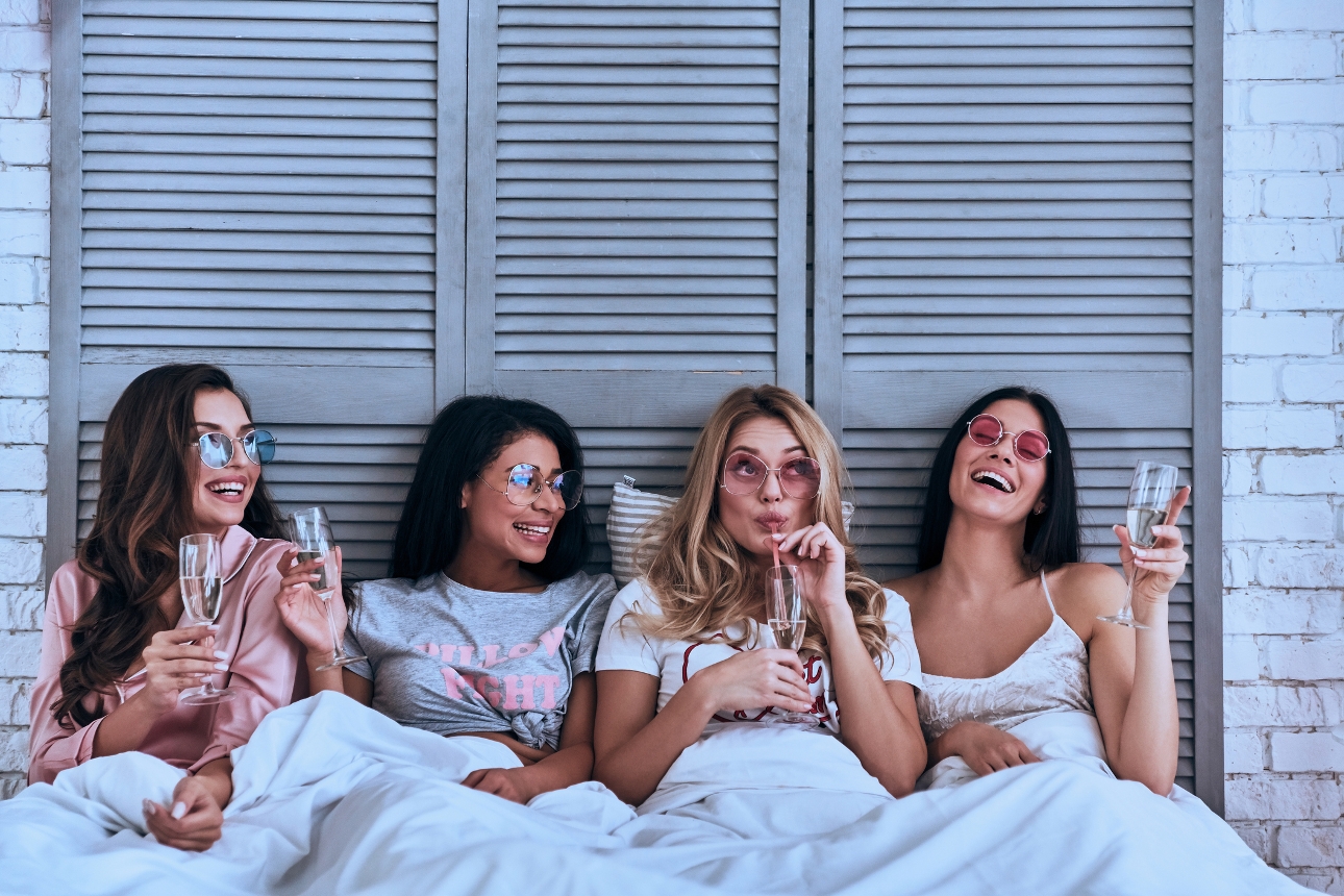 four women in bed in pjs with hen do props on