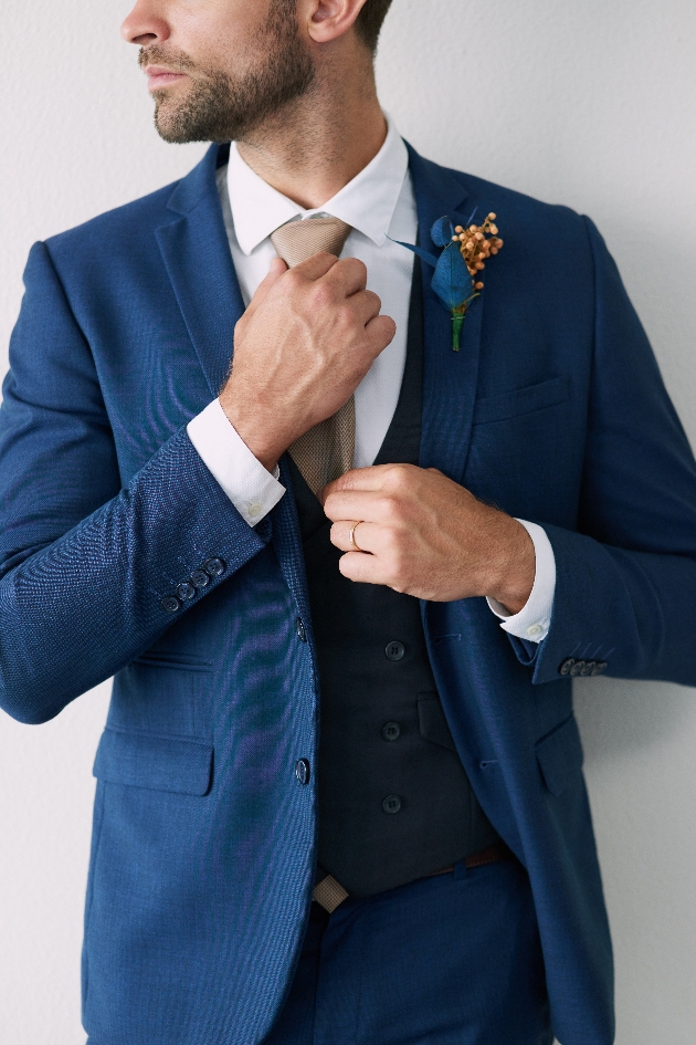Man wearing a blue suit fixing his tie