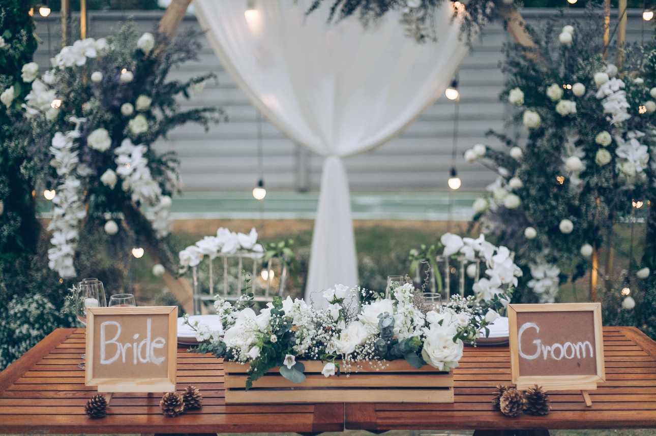 wooden table with bride and groom sign and flower in white and foliage all around it