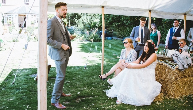 Groom giving his speech in marquee with guests sitting on haybales