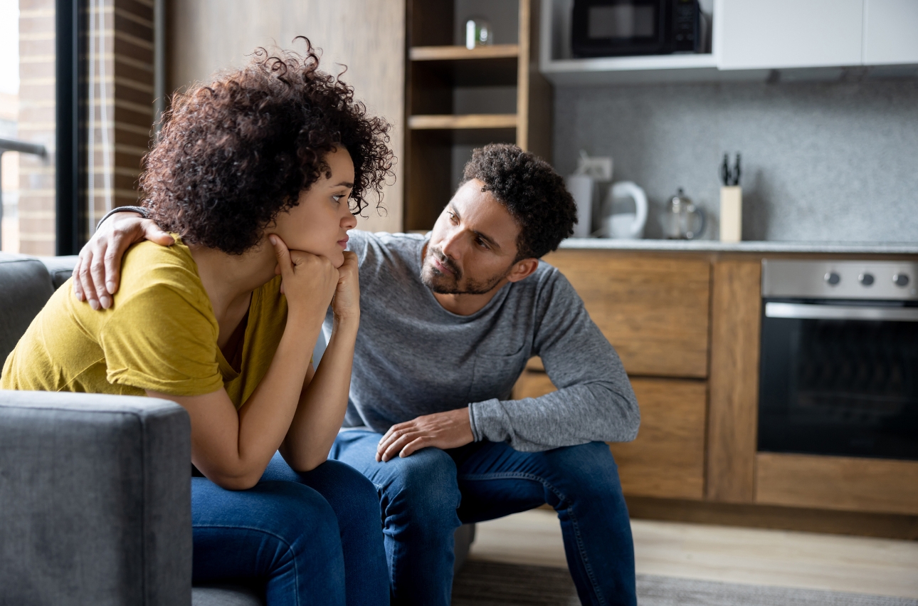 woman on sofa head in hands, man next to her arm around her