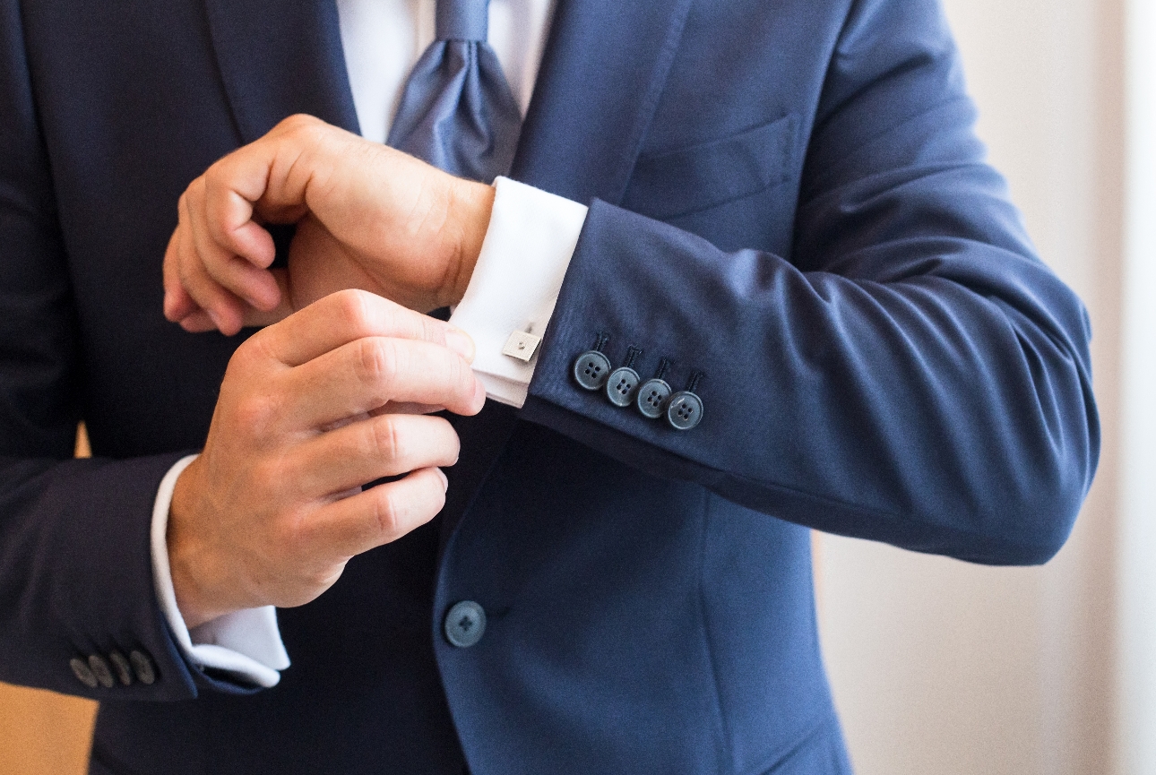 close up of man in blue suit adjusting cufflink in shirt