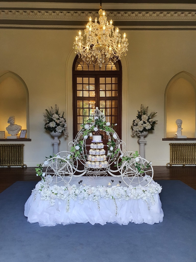 cinderella carriage cake stand in big historic venue surrounded by flowers