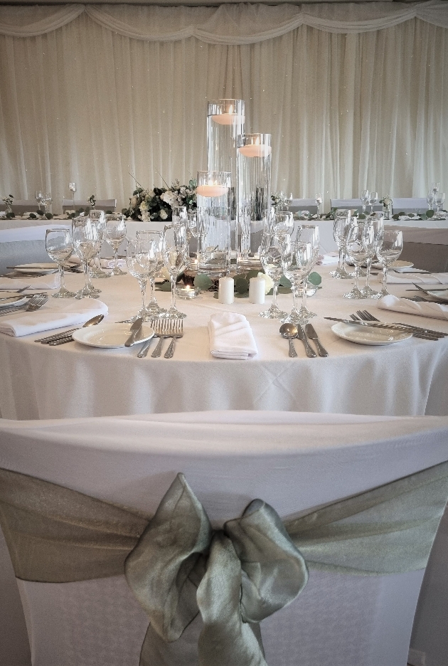 wedding breakfast table set up with white linen and green sash candles for centrepiece