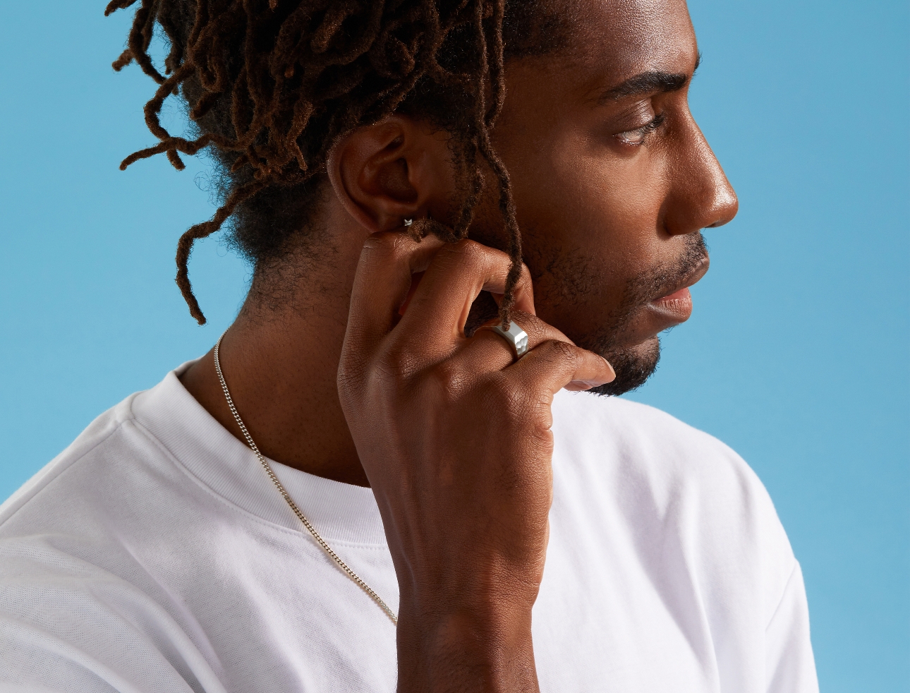 man in white tshirt wearing silver wedding band and touching his ear 