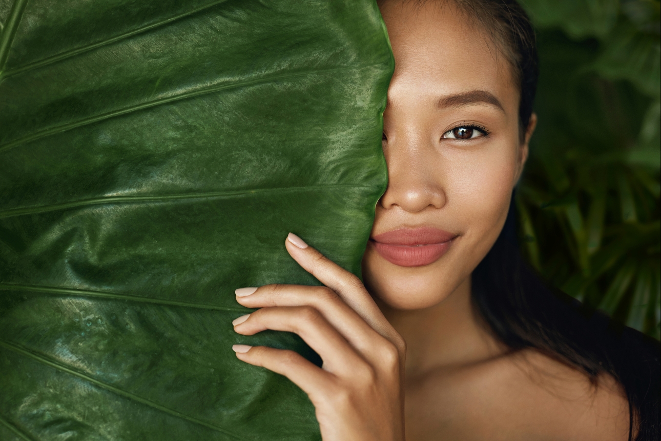 model with minimal makeup and a large leaf over half of her face
