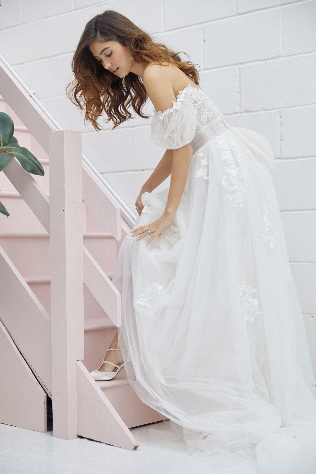 model in lace gown bending over to show her shoe under dress