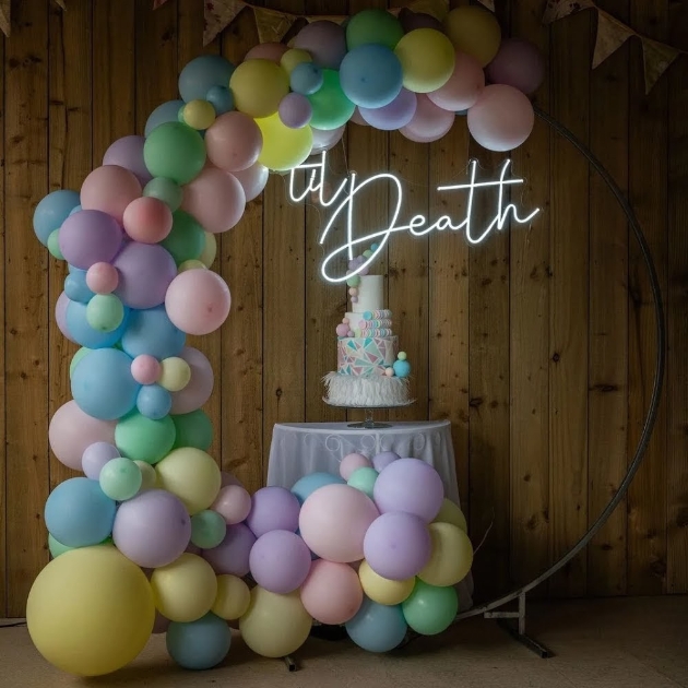 A four-tier cake sitting on a table surrounded by balloons and neon lights