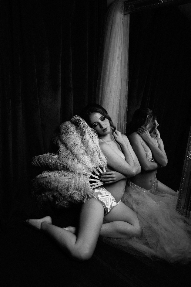 A black and white photo of a woman wearing underwear and holding a feathered fan