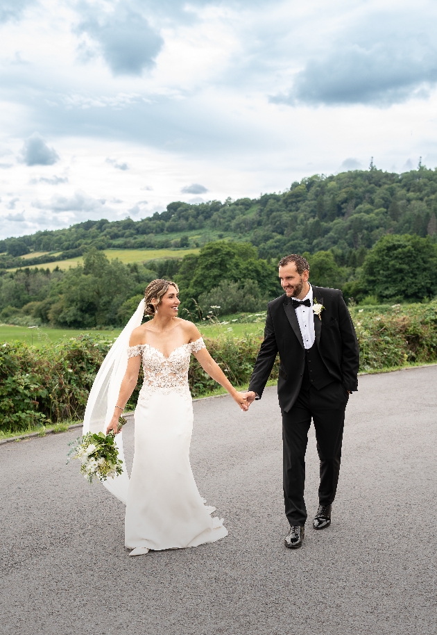 A bride and groom walking hand-in-hand on a road