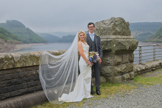 A bride and groom standing near a bridge
