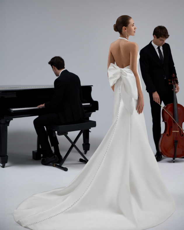 model in halterneck satin wedding dress with buttons down back and train with bown on back